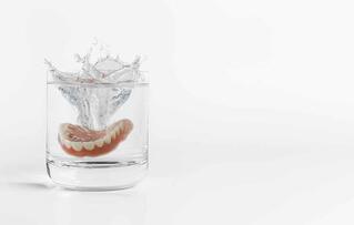 Dentures splash and falling drop into glass of water.