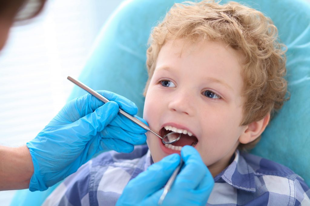 Young child receiving affordable dental care, getting an oral health exam by a dentist.