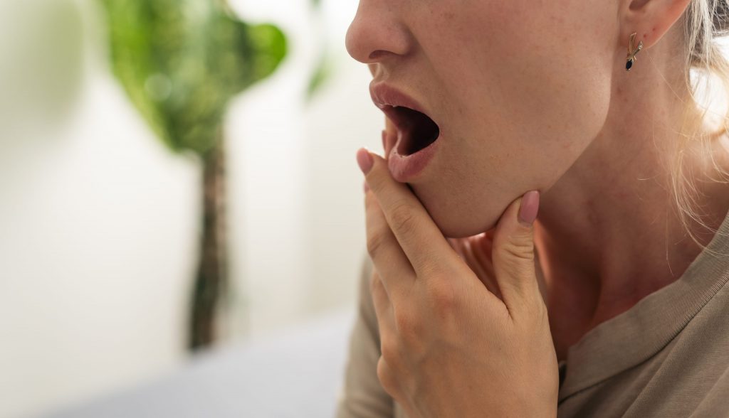 Woman feels tooth pain when she holds her mouth open, a sign she needs to make a dentist appointment for toothache relief. 