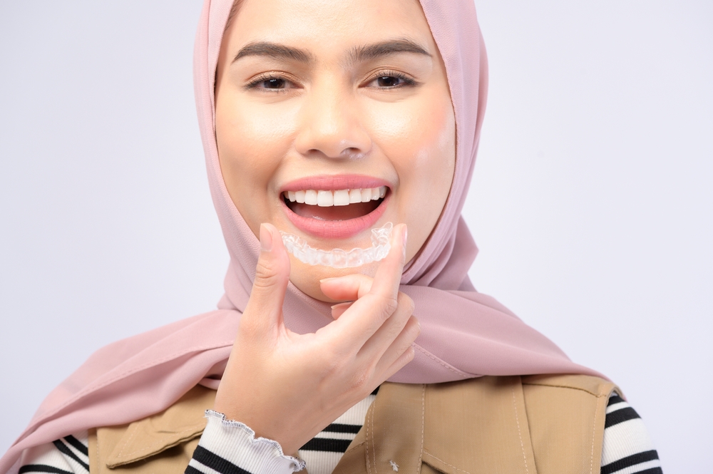  Woman in hijab smiles and removes invisible braces plastic aligner from mouth, a popular teeth straightening option. 