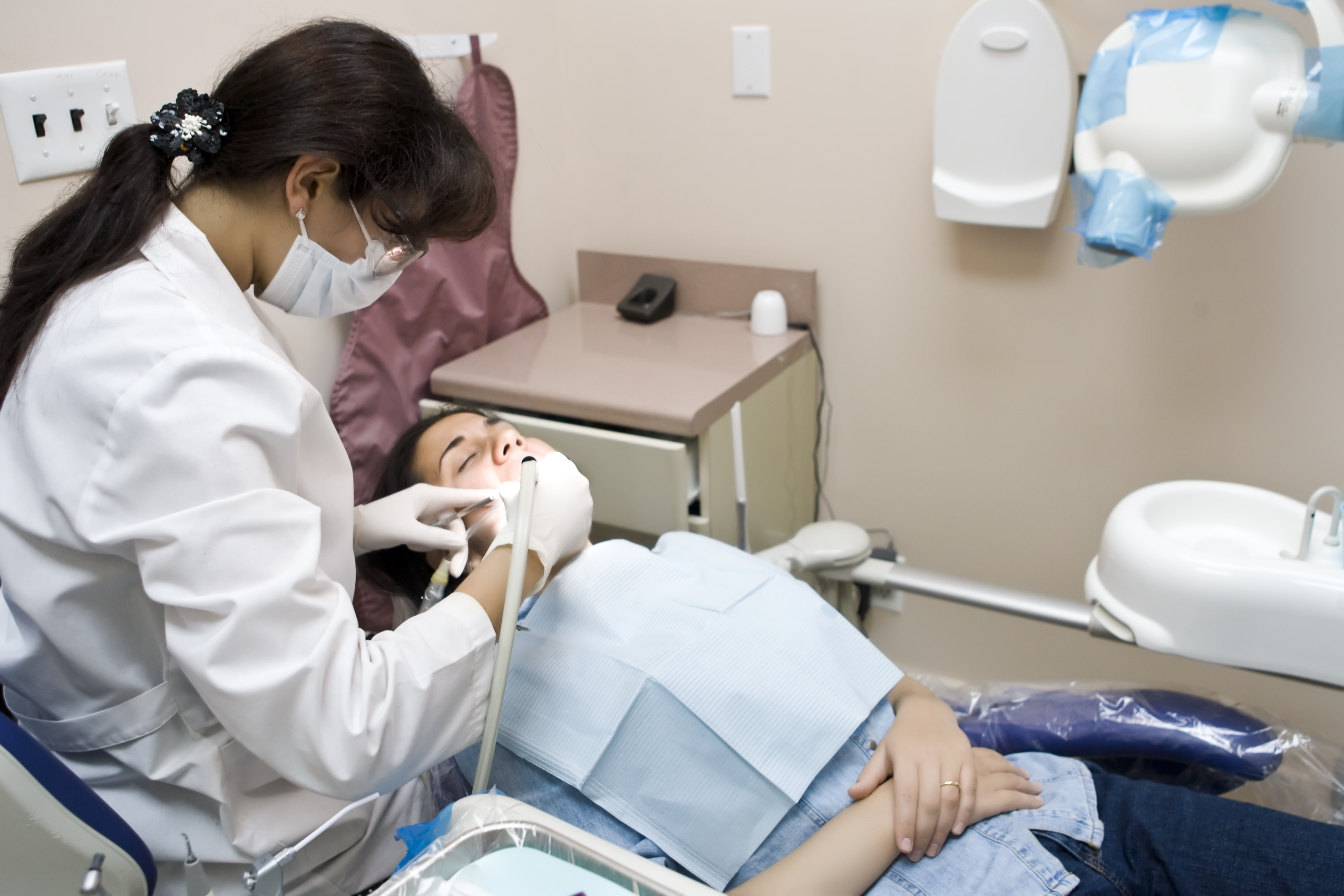  Masked and gloved periodontist treats gums of man reclining in dental chair.