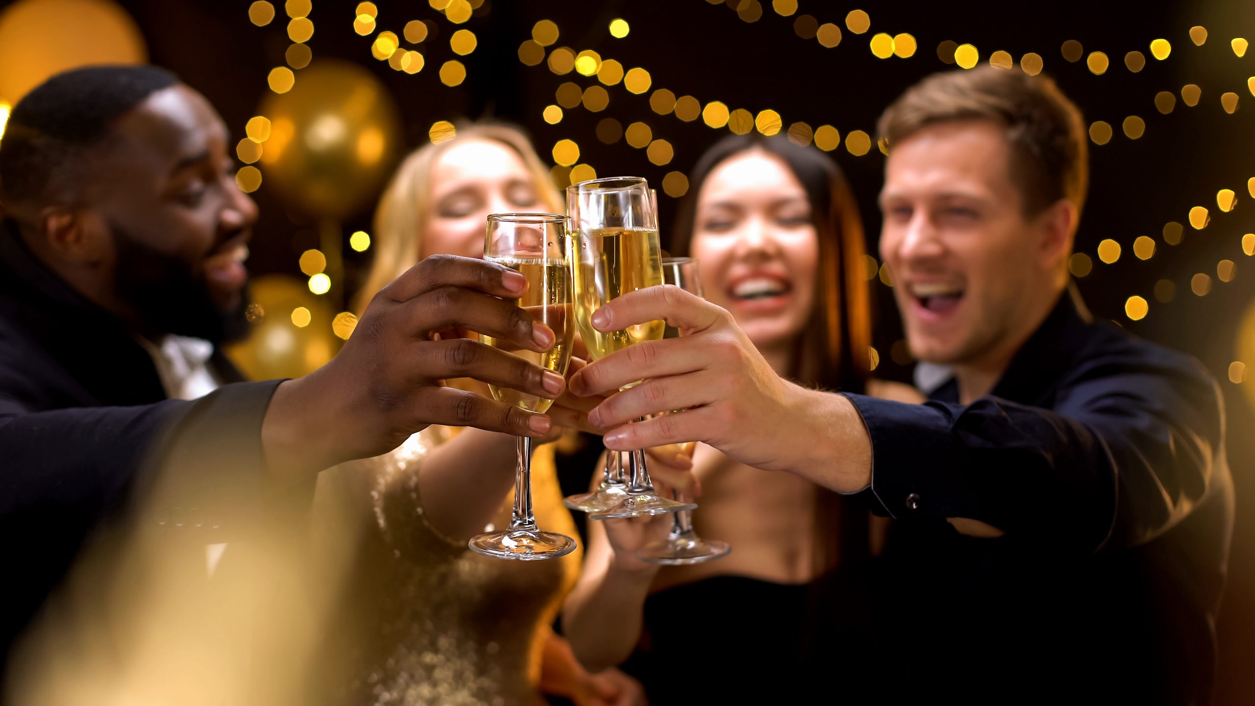 A group of four business colleagues toasts each other with glasses of champagne, surrounded by lights
