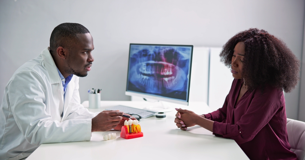  A top-rated dentist sits across a table from a patient in his office, reviewing an X-ray of her teeth on a lightbox. 