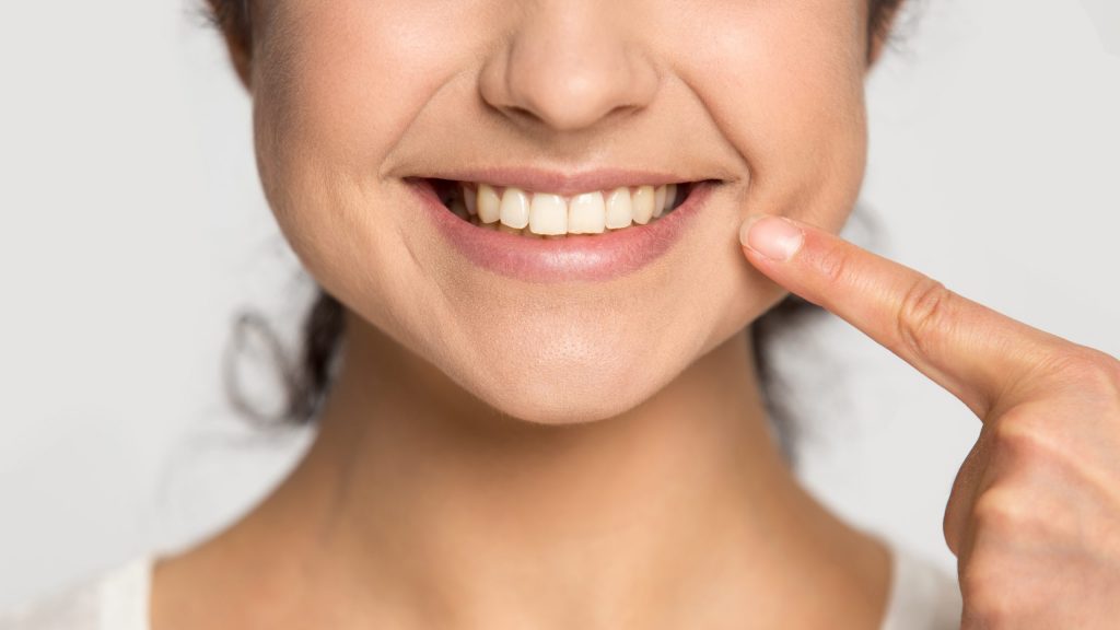 Close up happy smiling young woman pointing finger at healthy smile, demonstrating dental clinic service
