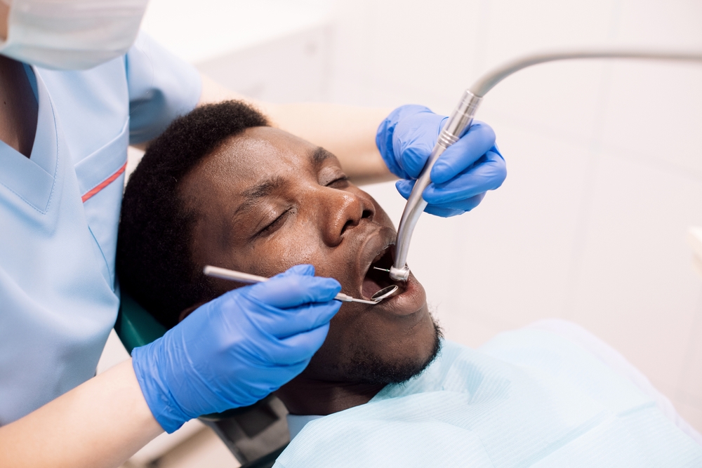 A young man sits in a dental chair while a dentist fixes a chipped tooth. 