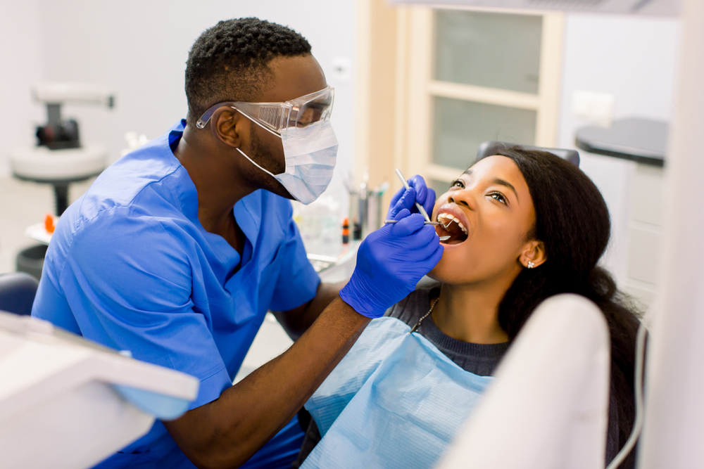 Dentist wearing mask, goggles, and gloves knows how to fix a broken tooth and inspects a damaged tooth in woman’s mouth.