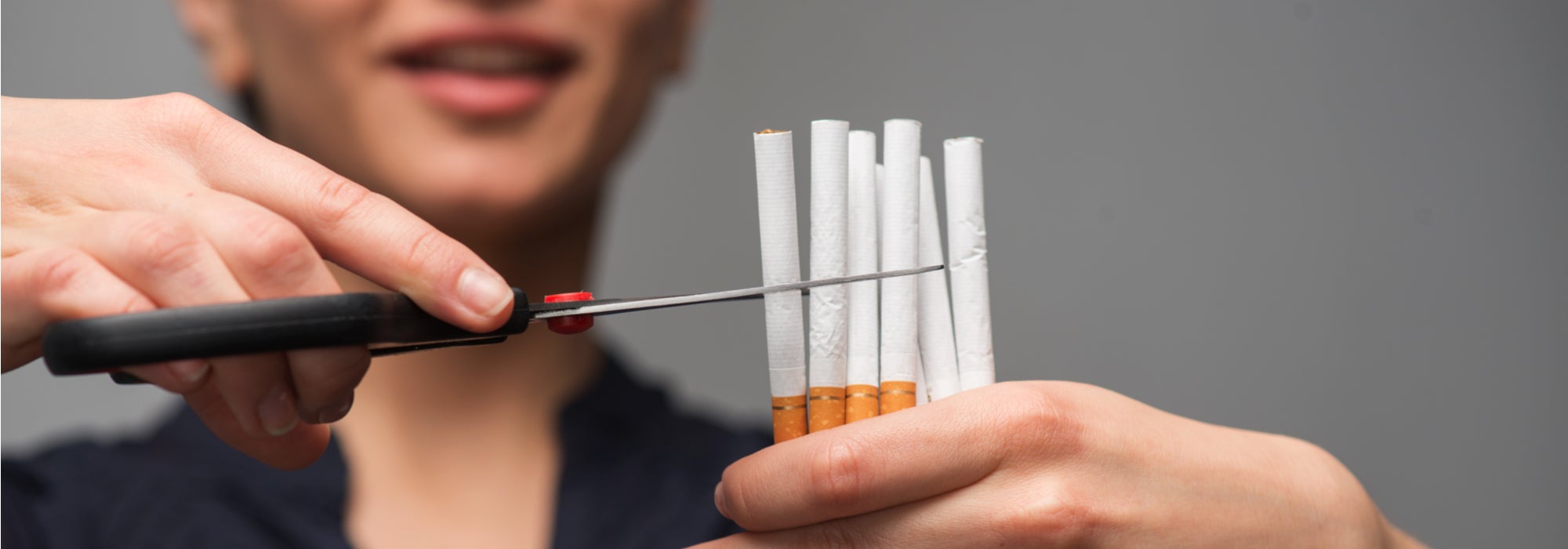 Young woman takes scissors to cut several cigarettes in half, showing her commitment to quit smoking.