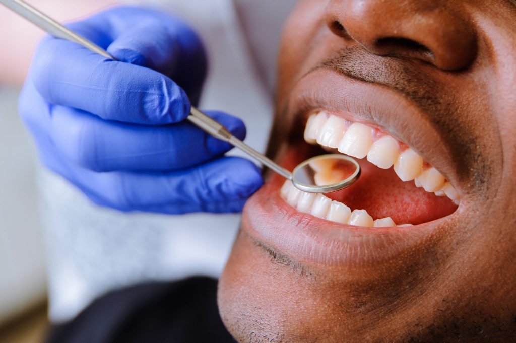 A dentist examines a Black man’s teeth. 