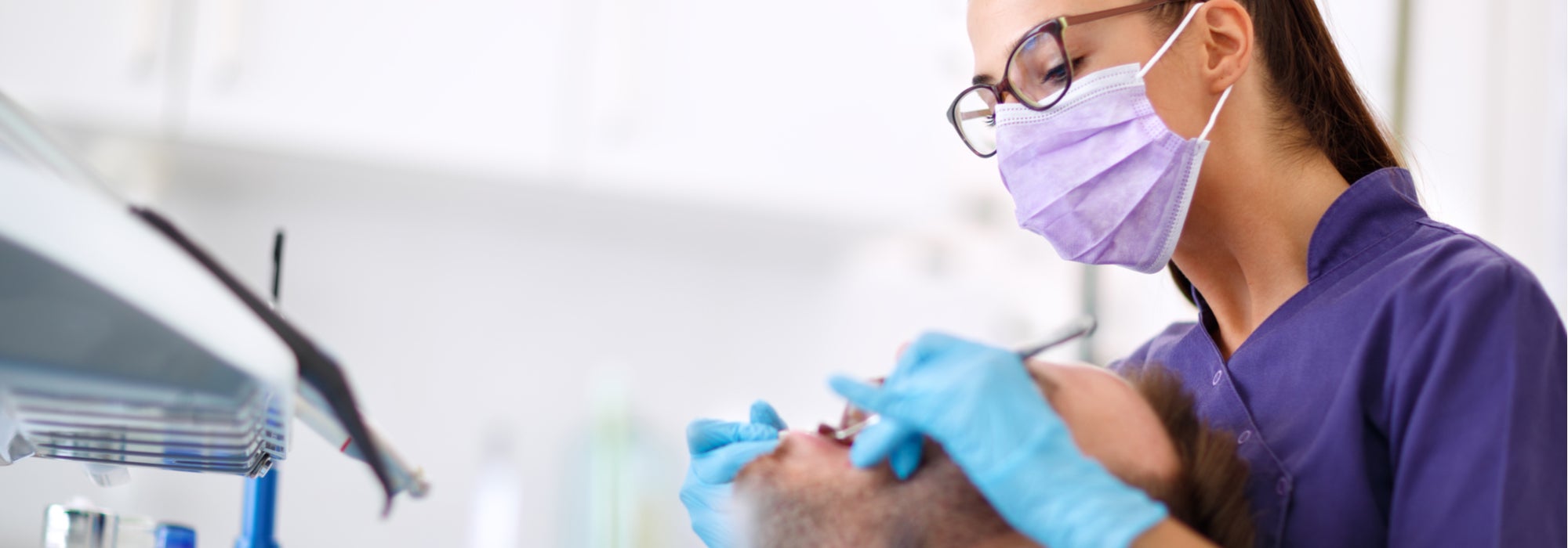 Young female dentist wearing a purple mask works on a patient’s mouth.