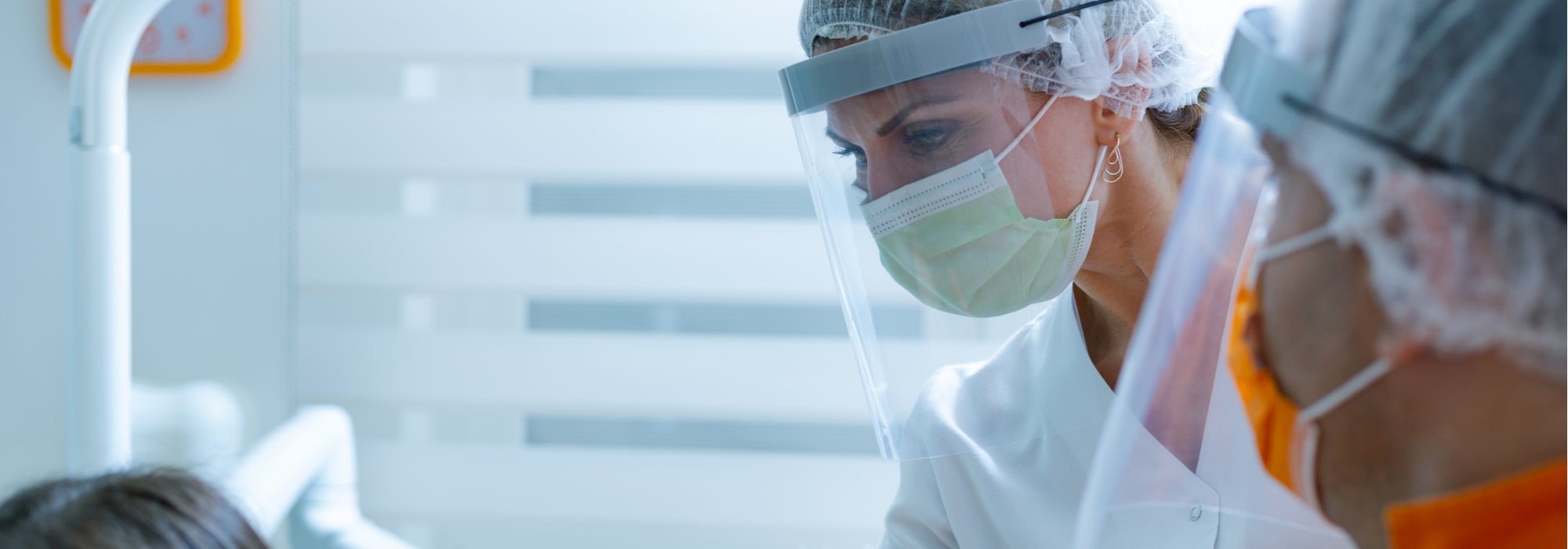 Female and male dental students in PPE provide dental care for a female patient with brown hair.