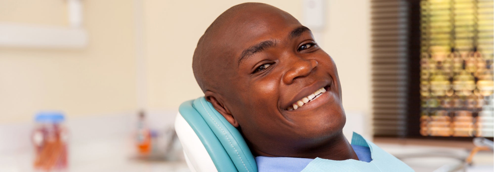 African-American male patient smiles as he sits in the dentist’s chair.