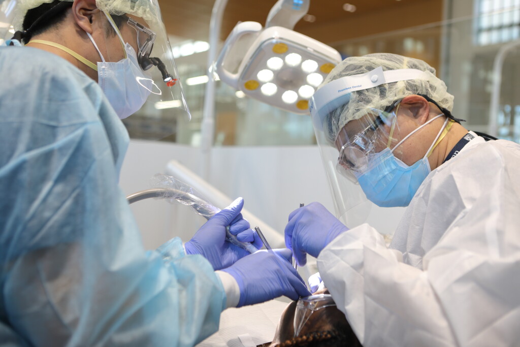 Two Penn Dental Medicine dentists wearing masks and facial shields perform oral surgery on Medicaid-covered patient.
