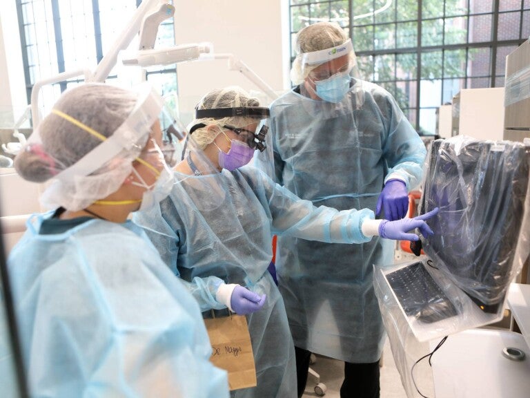 A Penn Dental Medicine faculty advisor and two student doctors consult a patient’s digital information on a monitor.