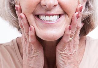 Smiling elderly woman with beauty face skin touch her cheeks with hands,show perfect clean white teeth,feel of happy satisfaction,good health,healthy body and happiness in life,facial expression.