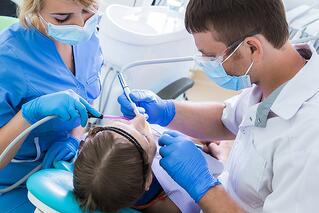 Two dentists in blue latex gloves check condition of a girl's teeth.
