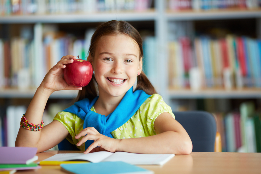 Young girl smiling while holding a apple.