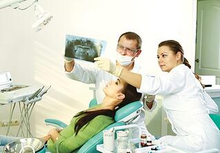 Two dentists examining the x-ray image while patient laying on the dental chair.