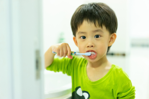 A boy try to brushes his teeth by himself in the restroom at night, before he go to bed.