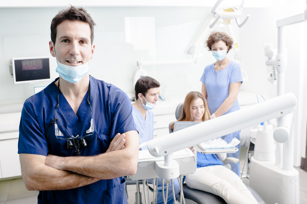 A portrait of a dentist with his team working in the background