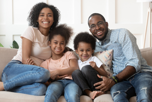 Happy black family nestles together on a couch. Left to right: Mom, young girl and boy, and Dad.