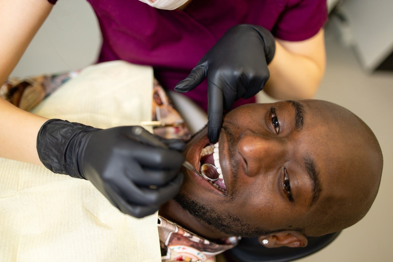 Man reclines in dental chair as dentist uses mirror to inspect placement of affordable porcelain crowns in his mouth.