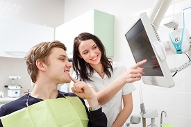 Young man on a review of a dentist, sitting in a chair. Dentist Explaining X-Ray on computer for patient in a dental clinic.