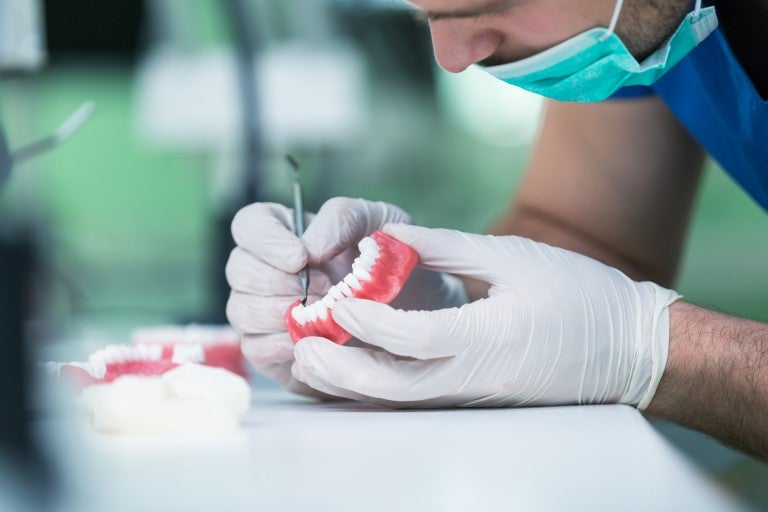 Dental prosthesis, dentures, prosthetics work. Prosthetics hands while working on the denture, false teeth, a study and a table with dental tools.