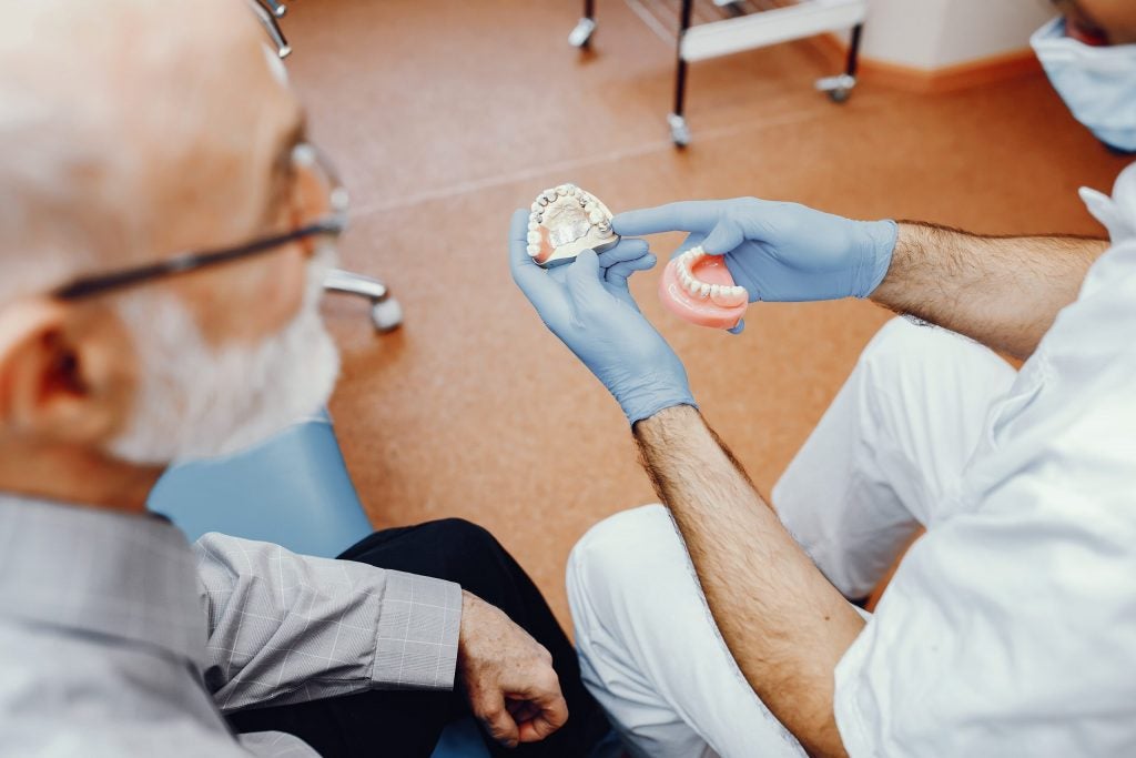 Doctor displaying affordable dentures for seniors to older man in a prosthodontics office