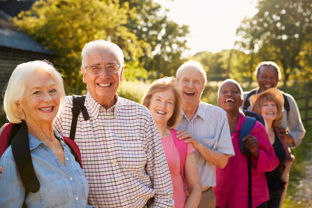 Senior friends with bright white smiles outdoors in a hiking group smiling and laughing.