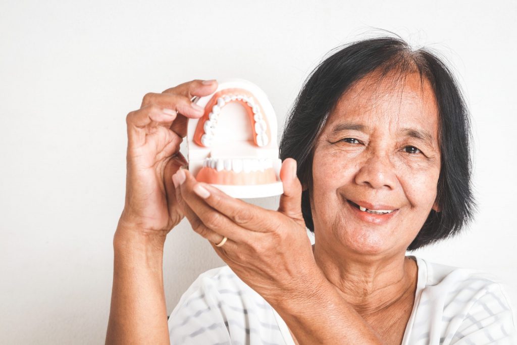 Close-up of woman smiling as she holds up her dentures.
