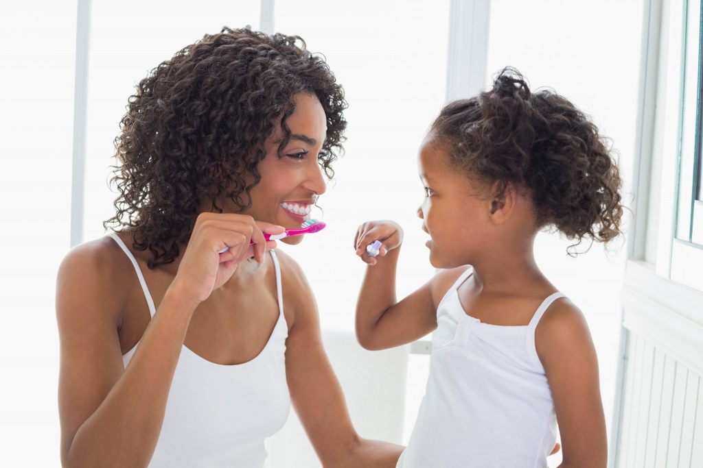 Mother and toddler daughter brush their teeth together. 