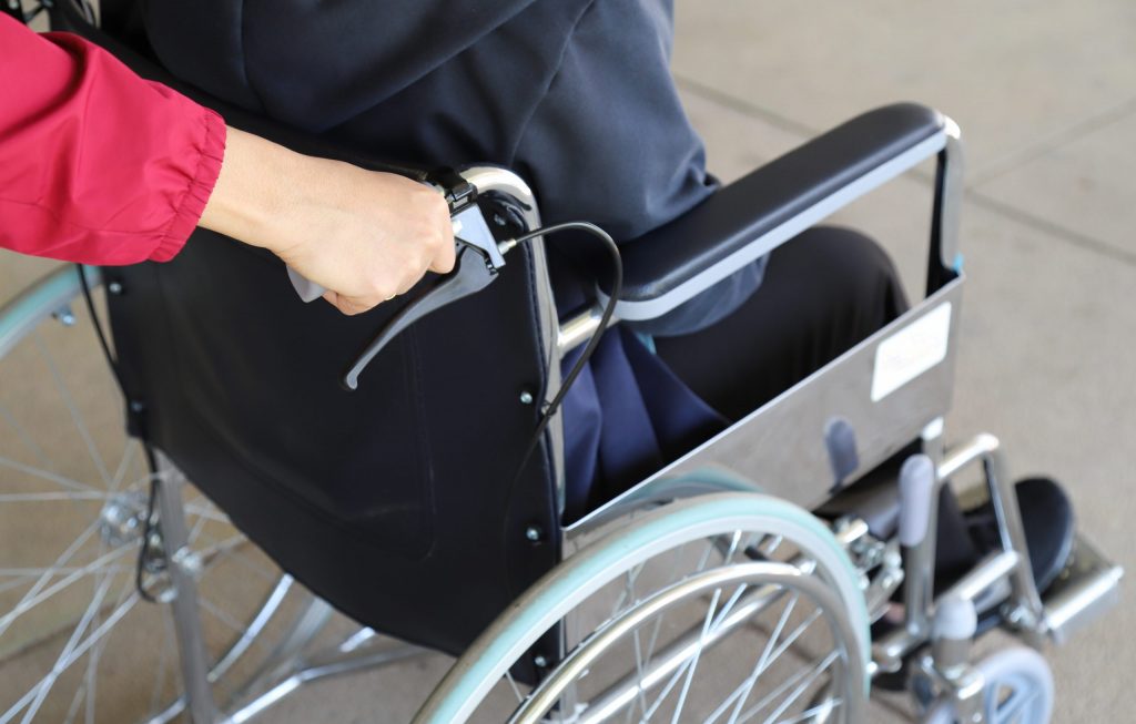 Close-up view of hands pushing a patient with disabilities in a wheelchair to visit a dentist for special needs patients.