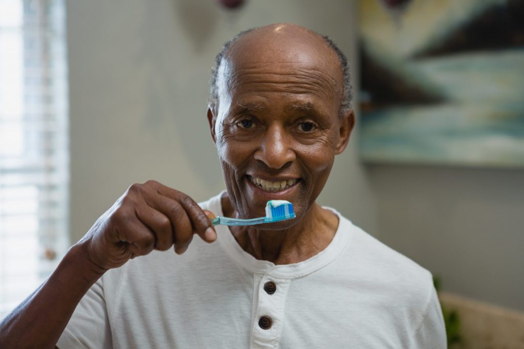 Smiling older man brushes his teeth at home.