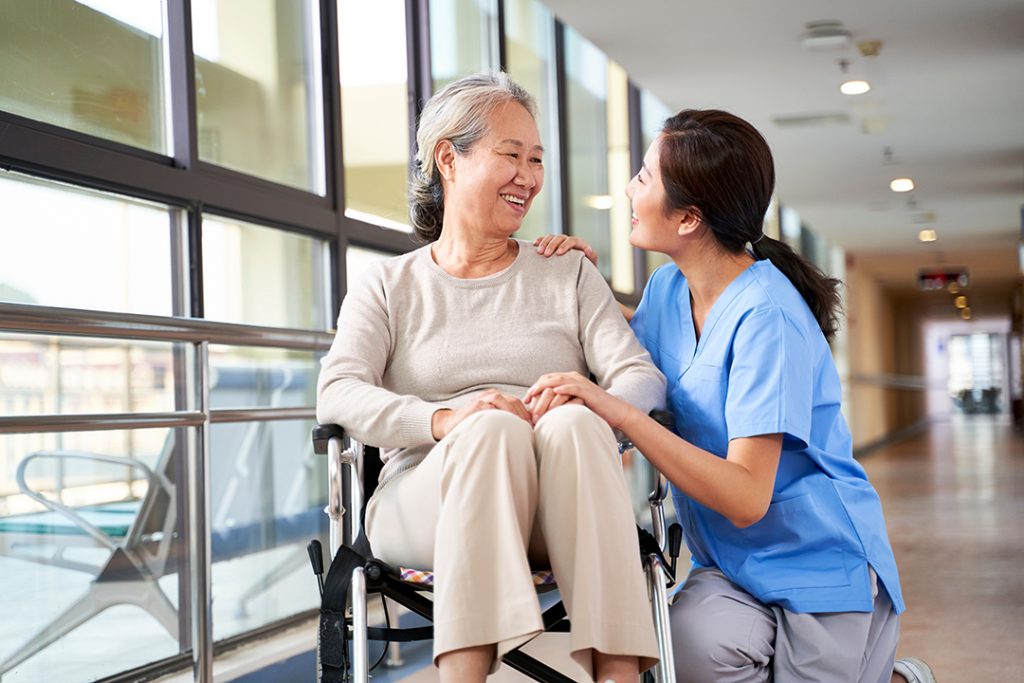  Woman in a wheelchair smiles at a caregiver in a medical facility. 