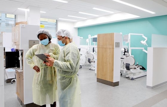 Two dentists in scrubs and masks in the open bay at the Personalized Care Suite confer about Down syndrome dental issues.