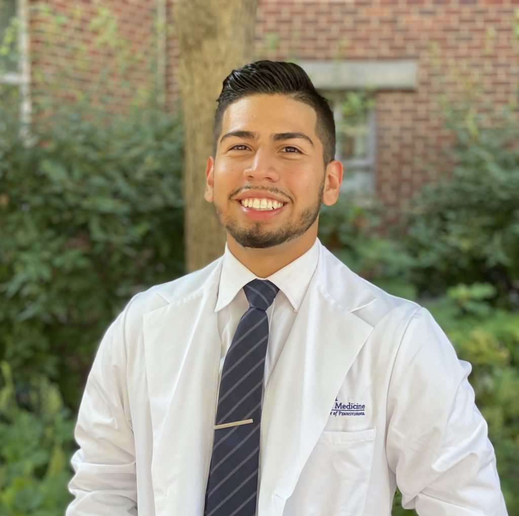 Third-year Penn Dental Medicine student dentist Paul Espiritu, wearing white dental jacket, poses for outdoor photo on campus.