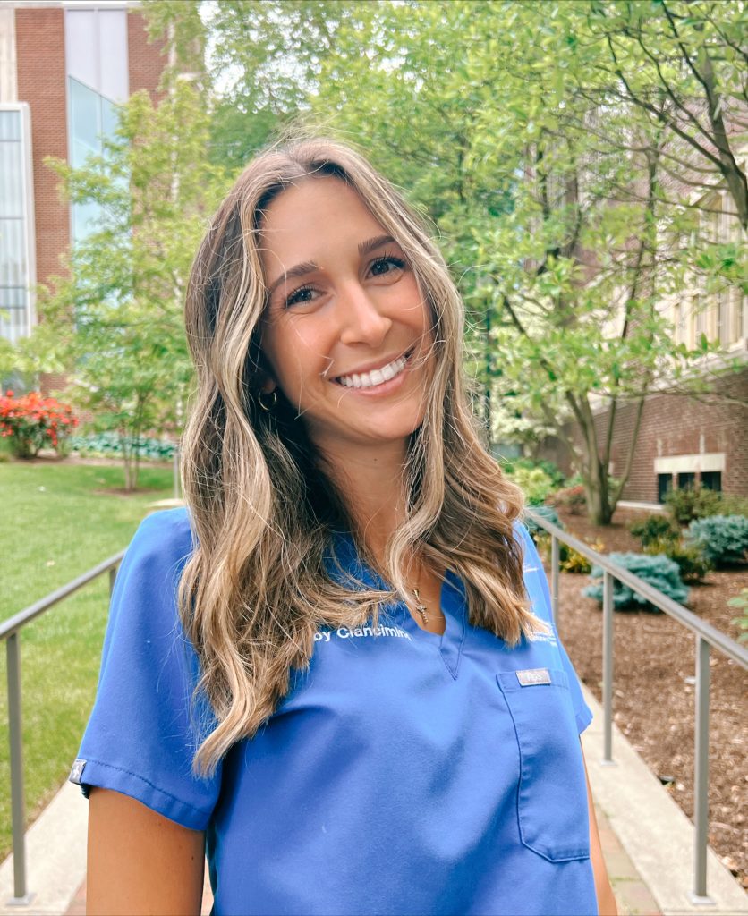 Third-year Penn Dental Medicine student dentist Gabby Ciancimino, wearing scrubs, poses for outdoor photo on campus.