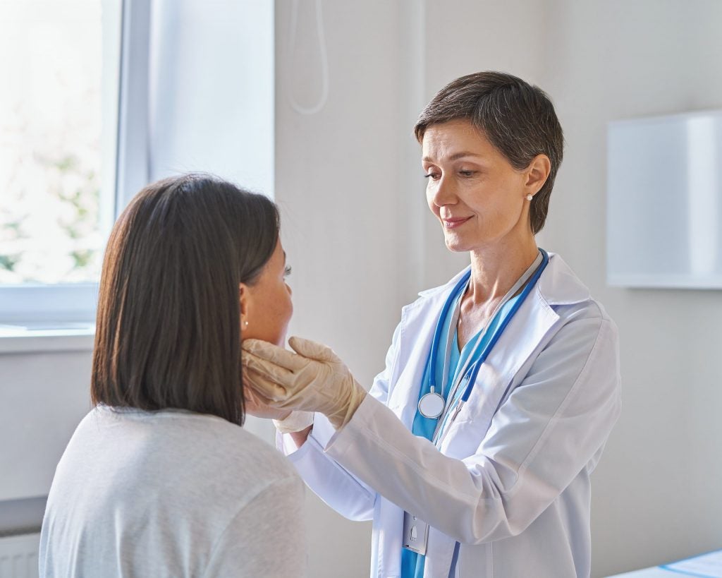 Doctor wearing gloves feels neck of woman in office, deciding whether patient needs to consult a dentist for cancer patients.