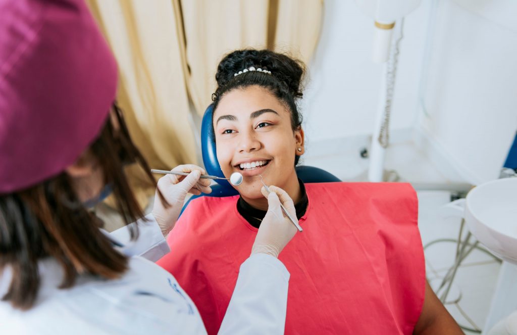 A patient in dental chair smiles at her dentist as dentist prepares to use a scalpel and mirror.