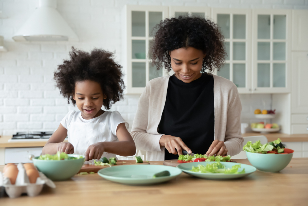 A mother and daughter work at a kitchen island, making a salad filled with dental superfoods.