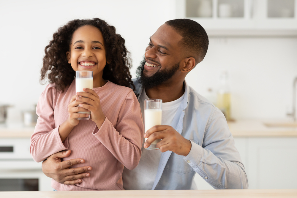 A father and daughter are smiling as they drink milk, a dental superfood.