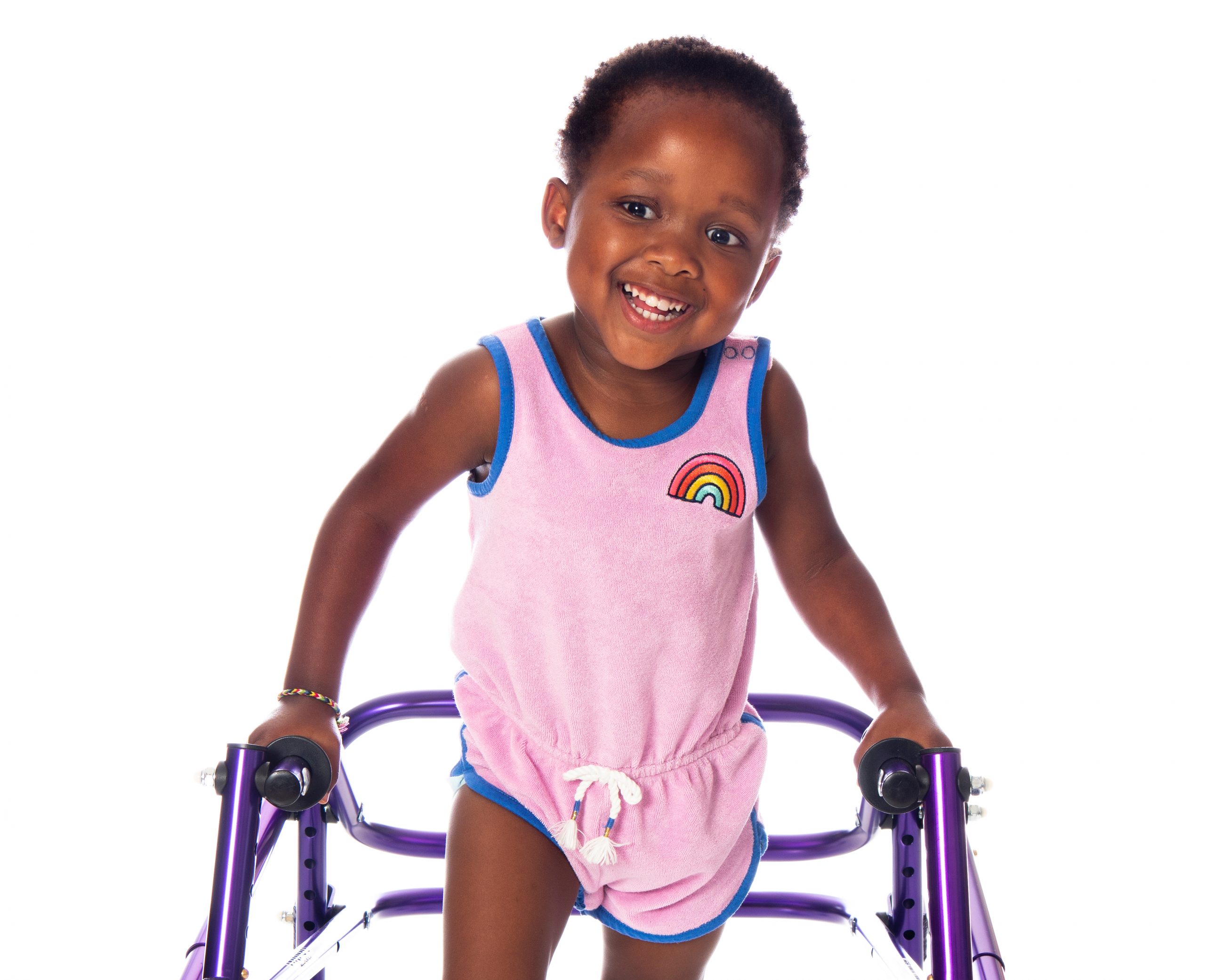 A toddler girl with cerebral palsy smiles a big, bright smile as she takes steps using her walker.