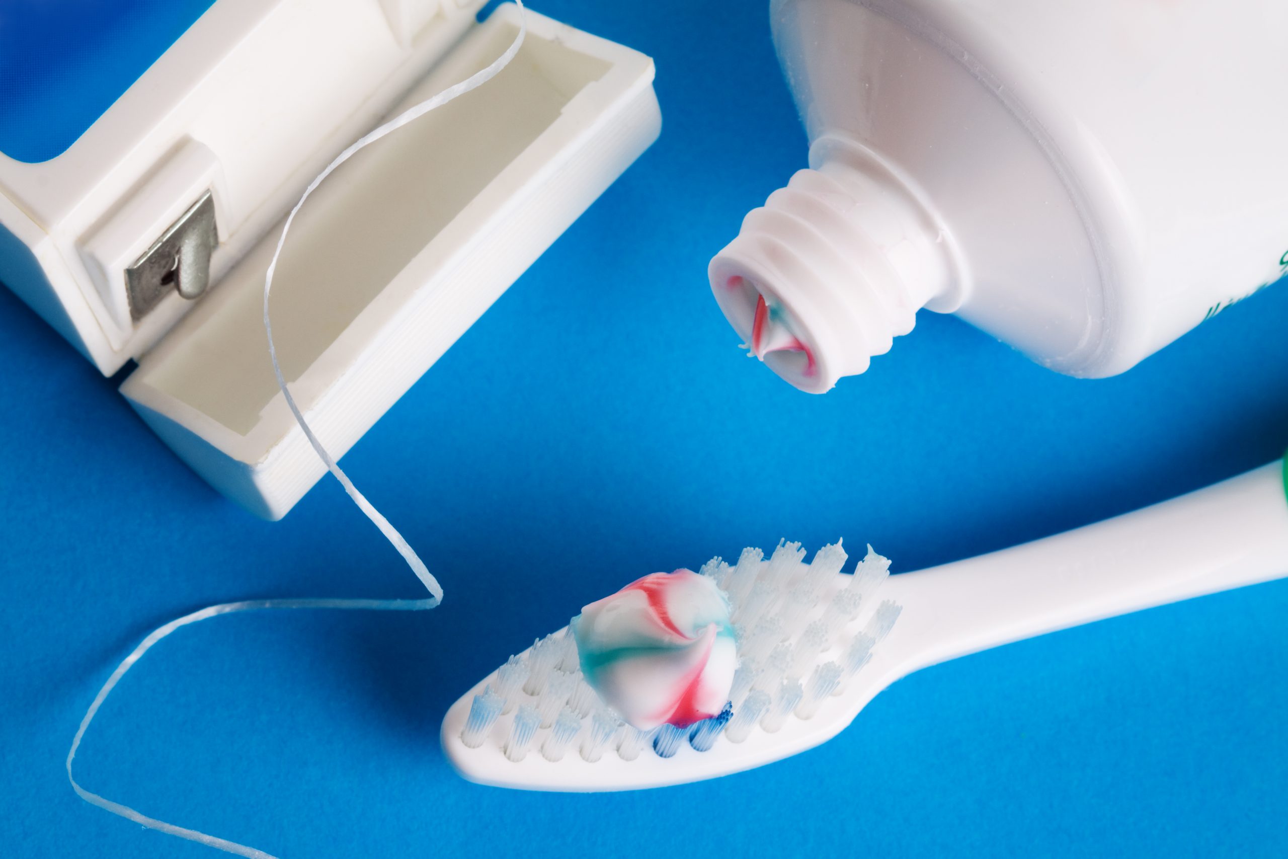 Dental floss, a toothbrush with striped toothpaste, and a toothpaste tube illustrate the need for great oral health.