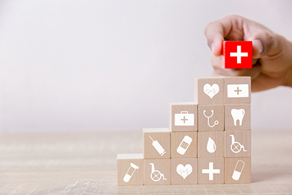  A person arranges wood blocks with health-care images in stacks in rising rows with a red medical icon block at the top. 