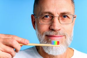 A man holds a rainbow-colored toothbrush illustrating oral health disparity affecting members of the LGTBQ+ community. 