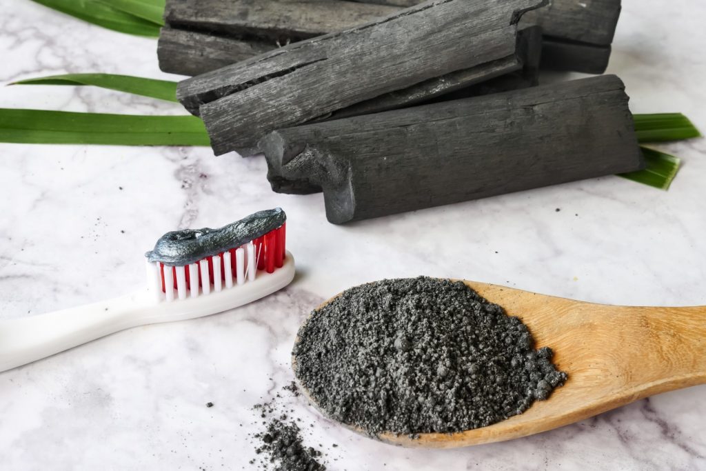 Toothpaste with charcoal toothpaste is on a granite counter next to activated charcoal powder and fragments of black wood. 