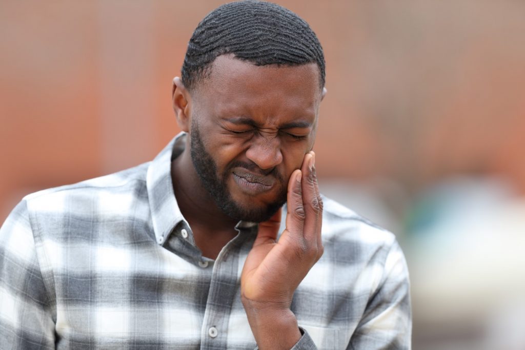 A young man frowns as he holds his hand to his painful tooth and mouth.