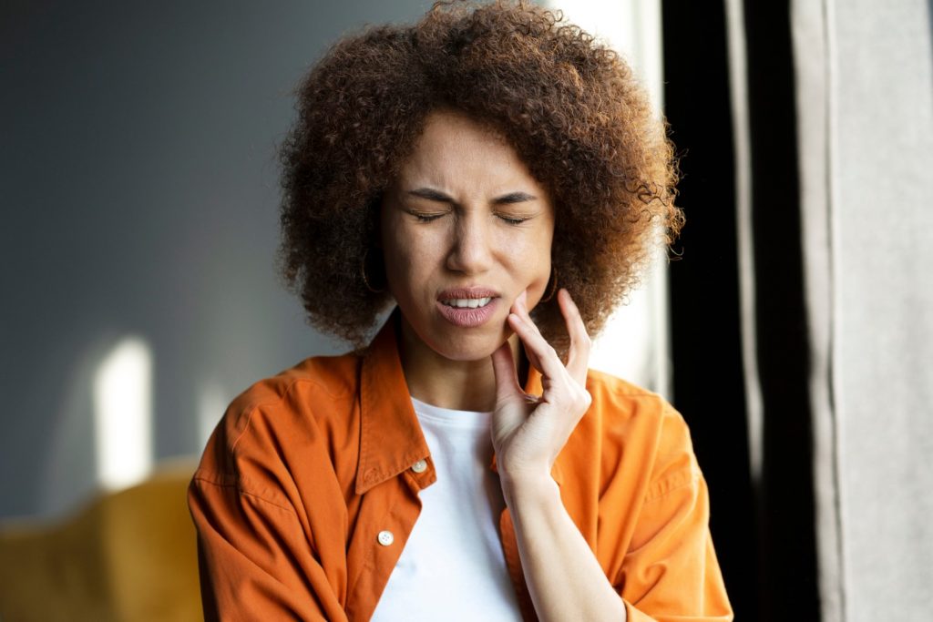 A woman winces as she holds her left hand to her mouth, indicating she has a toothache, one of the most common dental problems.