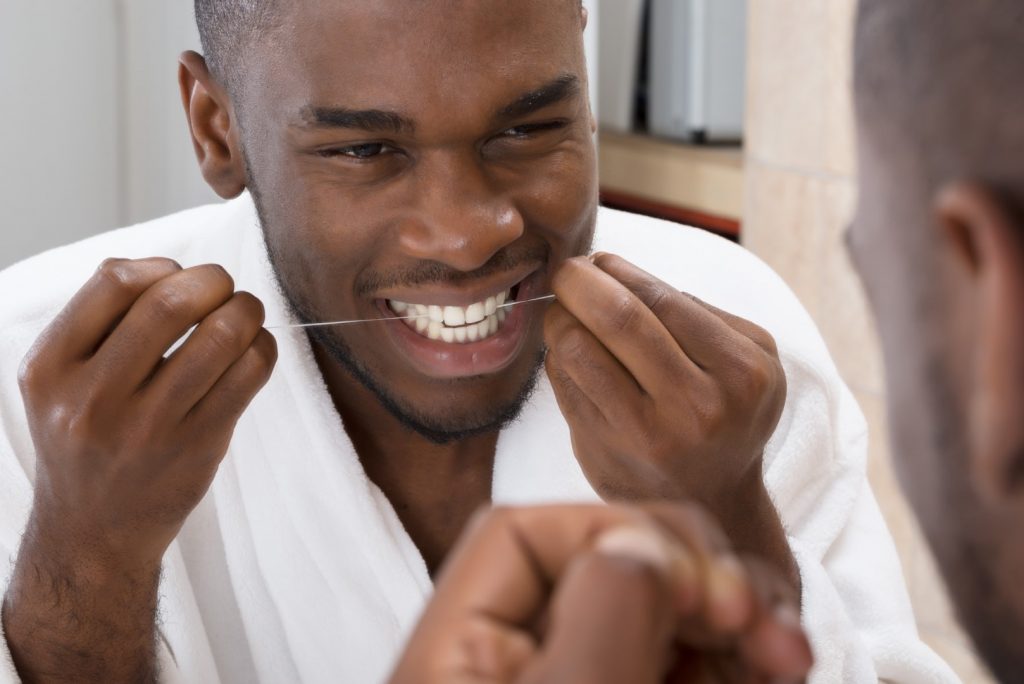 A young man looks in the mirror as he flosses his teeth as part of preventive dentistry.