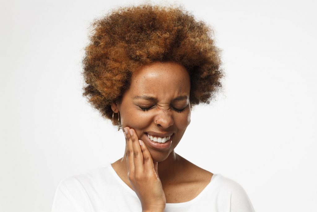 A woman winces as she holds her right hand to her cheek, wondering, “Why are my teeth sensitive?” 